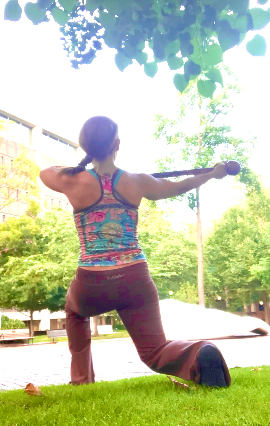 Woman doing a fitness exercise with a club outdoors; blue, brown, green colors.