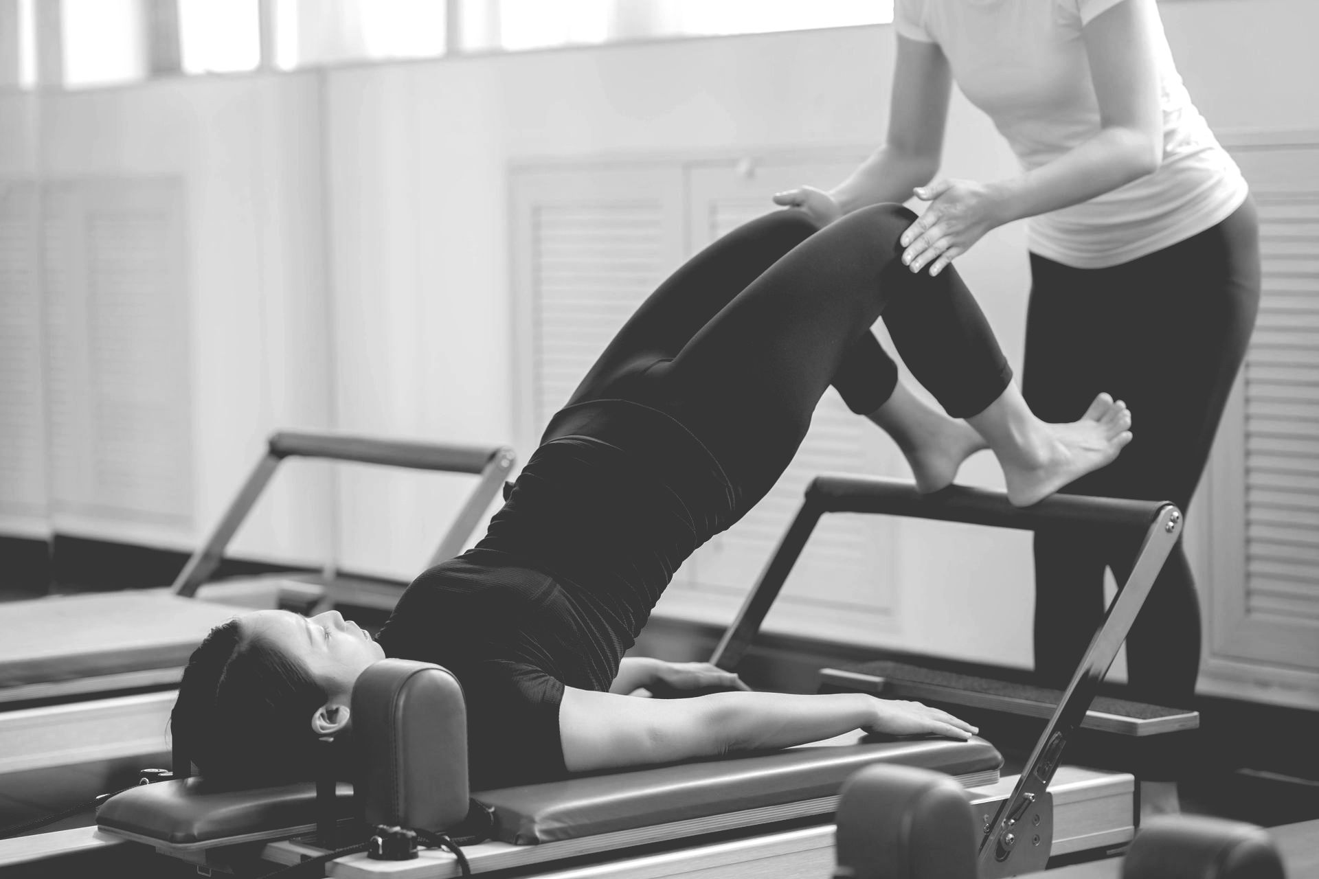 Woman doing Pilates exercise with instructor's assistance on a reformer machine.