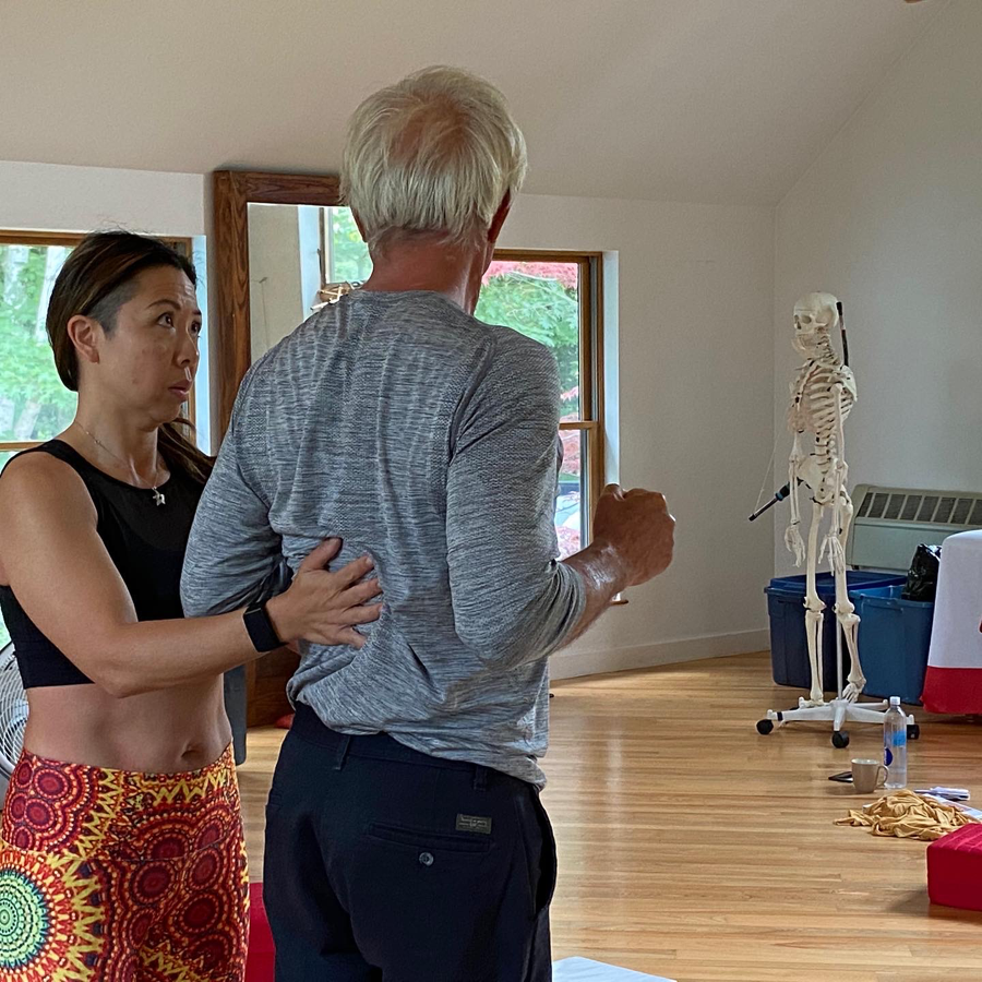 Woman assisting a person with lower back posture in a room with a skeleton model.