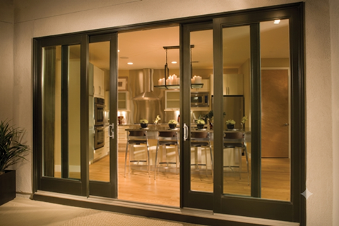 Open glass doors revealing a warmly lit modern kitchen and dining area