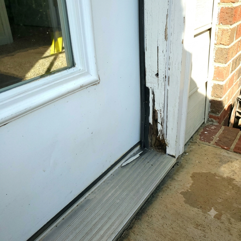 Worn white door frame with peeling paint beside a brick wall and concrete step threshold.