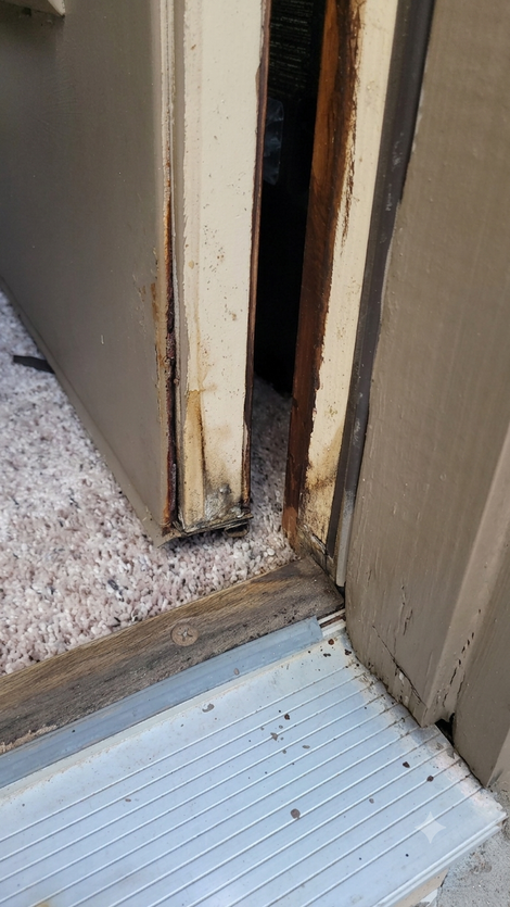 Close-up of a damaged door frame with a narrow gap and worn trim beside a threshold strip.