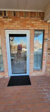 Brick house entry with glass door, side window, and black doormat on a tiled porch