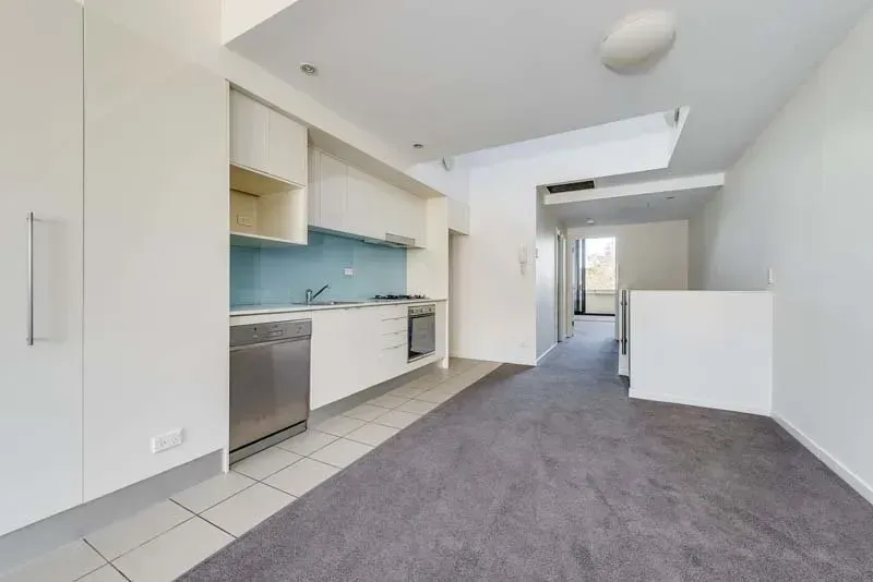 Small kitchen with white cabinets, stainless steel appliances, and gray carpet.