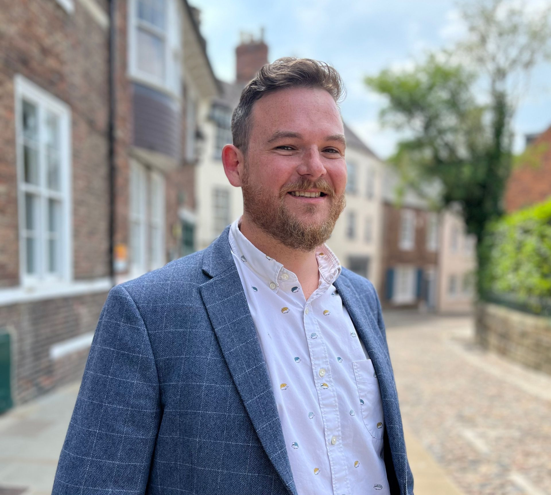 Smiling man in a blue blazer standing on a cobblestone street outdoors
