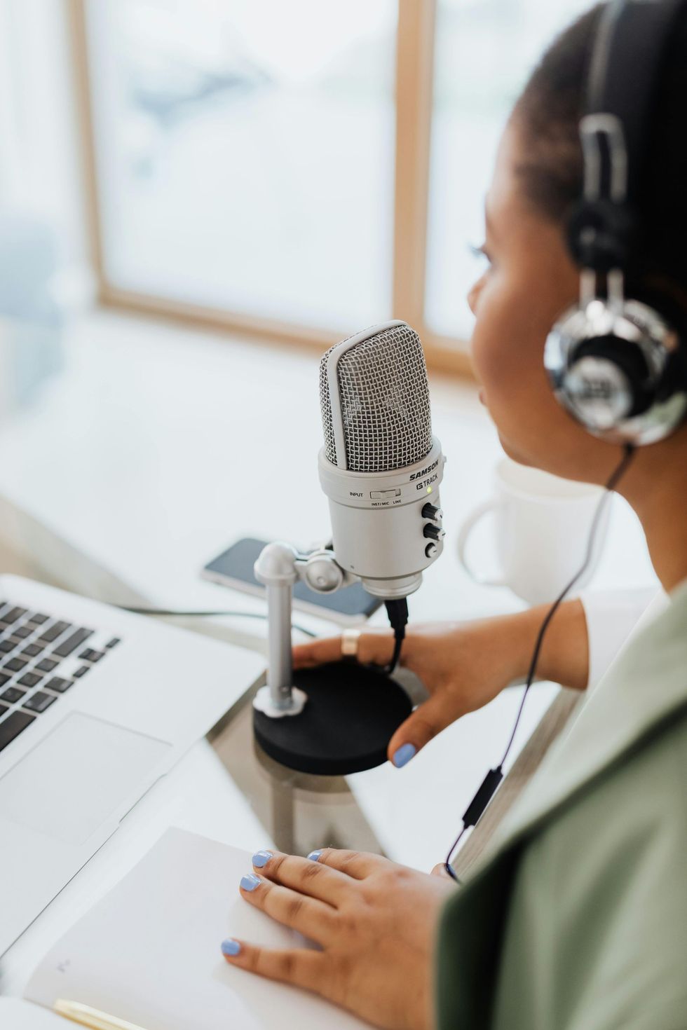 Person wearing headphones speaking into a studio microphone beside a laptop