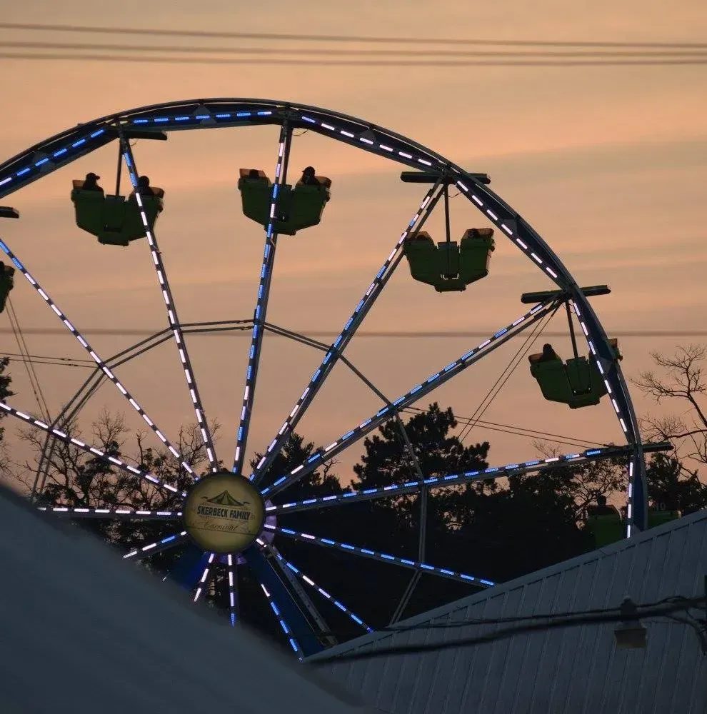 A Ferris wheel lit with blue LED lights against a sunset sky, with passenger cars visible at various heights.