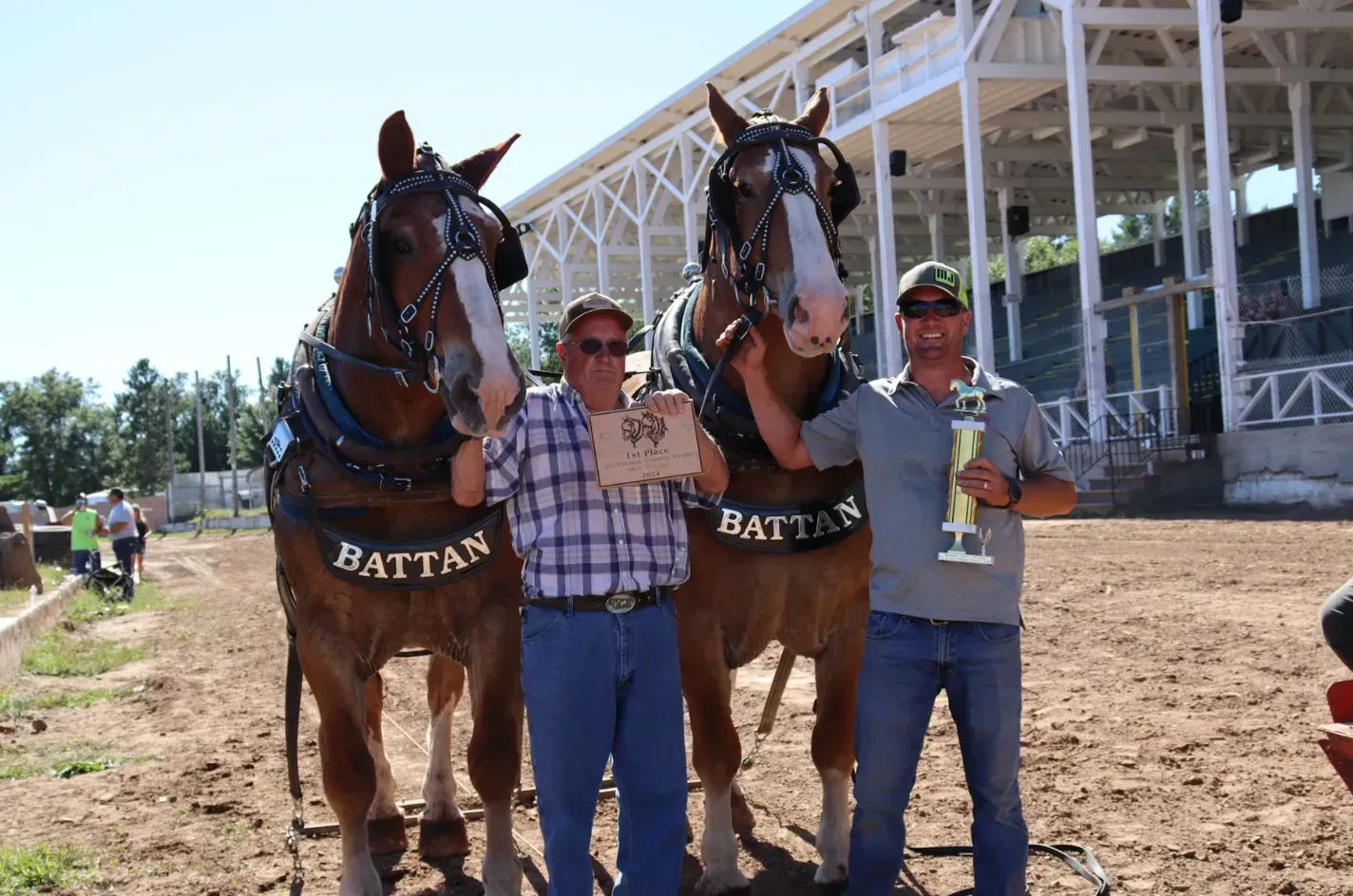 Two people stand with award ribbons between two draft horses labeled