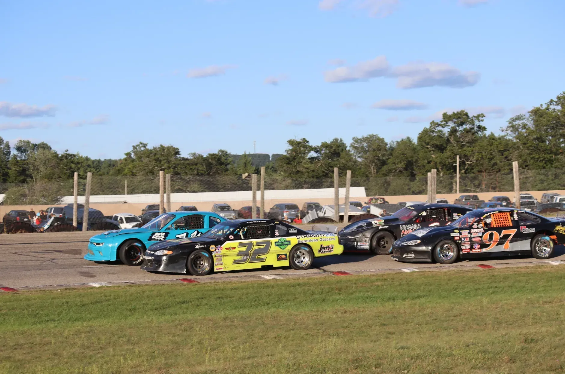 Four race cars driving on a track, including a blue car, a yellow car numbered 22, and a black car numbered 97.