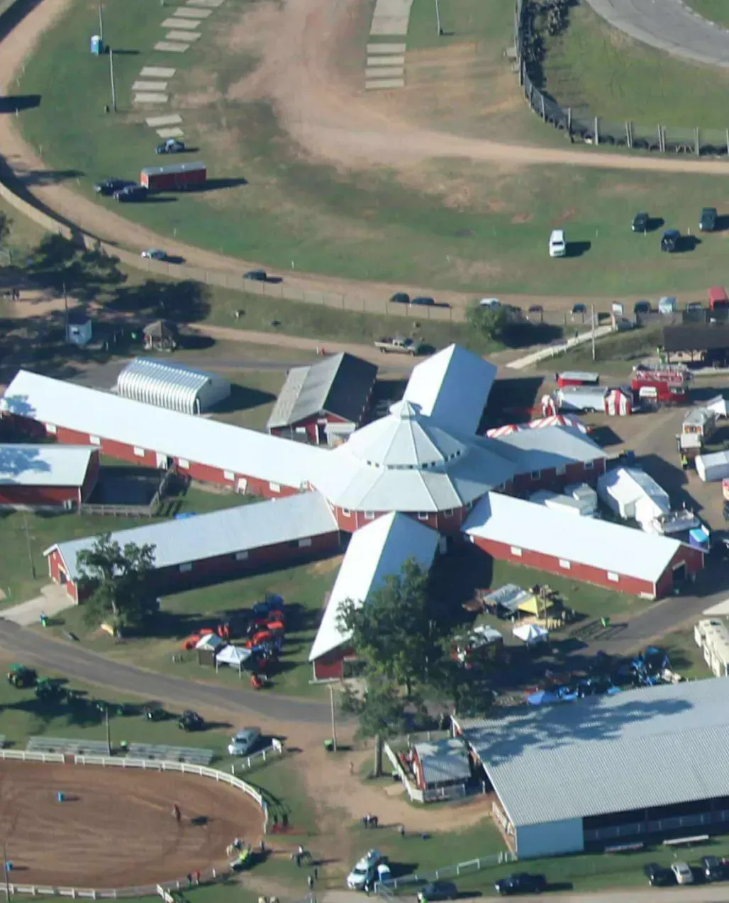 Aerial view of a unique, star-shaped red barn complex with white roofs, surrounded by dirt tracks and parking areas.