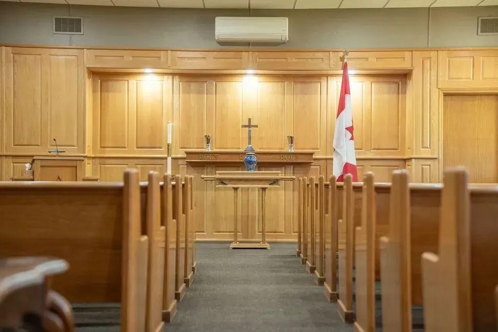 Empty courtroom with wooden benches, judge’s bench, and a Canadian flag at the front.