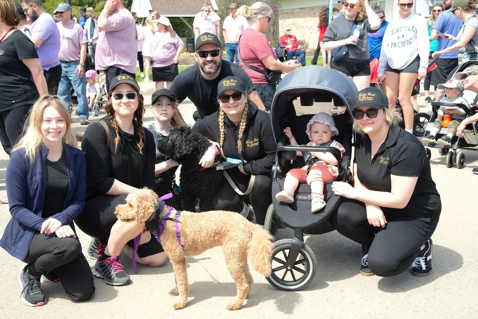Group of people posing outdoors; a child sits in a stroller, and a tan dog stands in front.