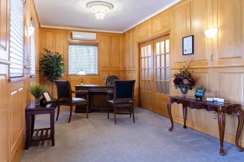 Wood-paneled waiting room with chairs, desk, potted plants, and framed wall art
