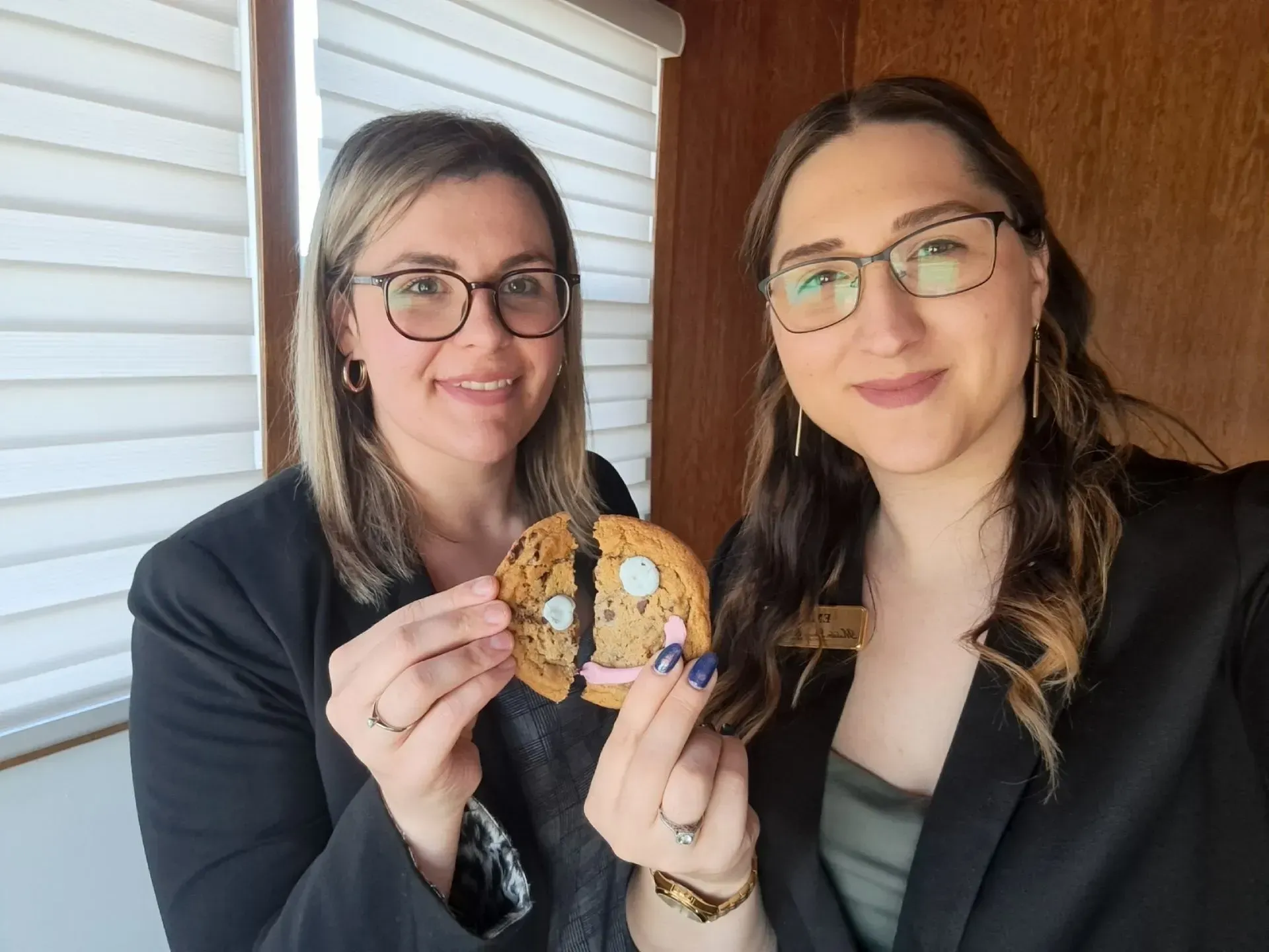 Two people smiling and holding a decorated cookie indoors by a window