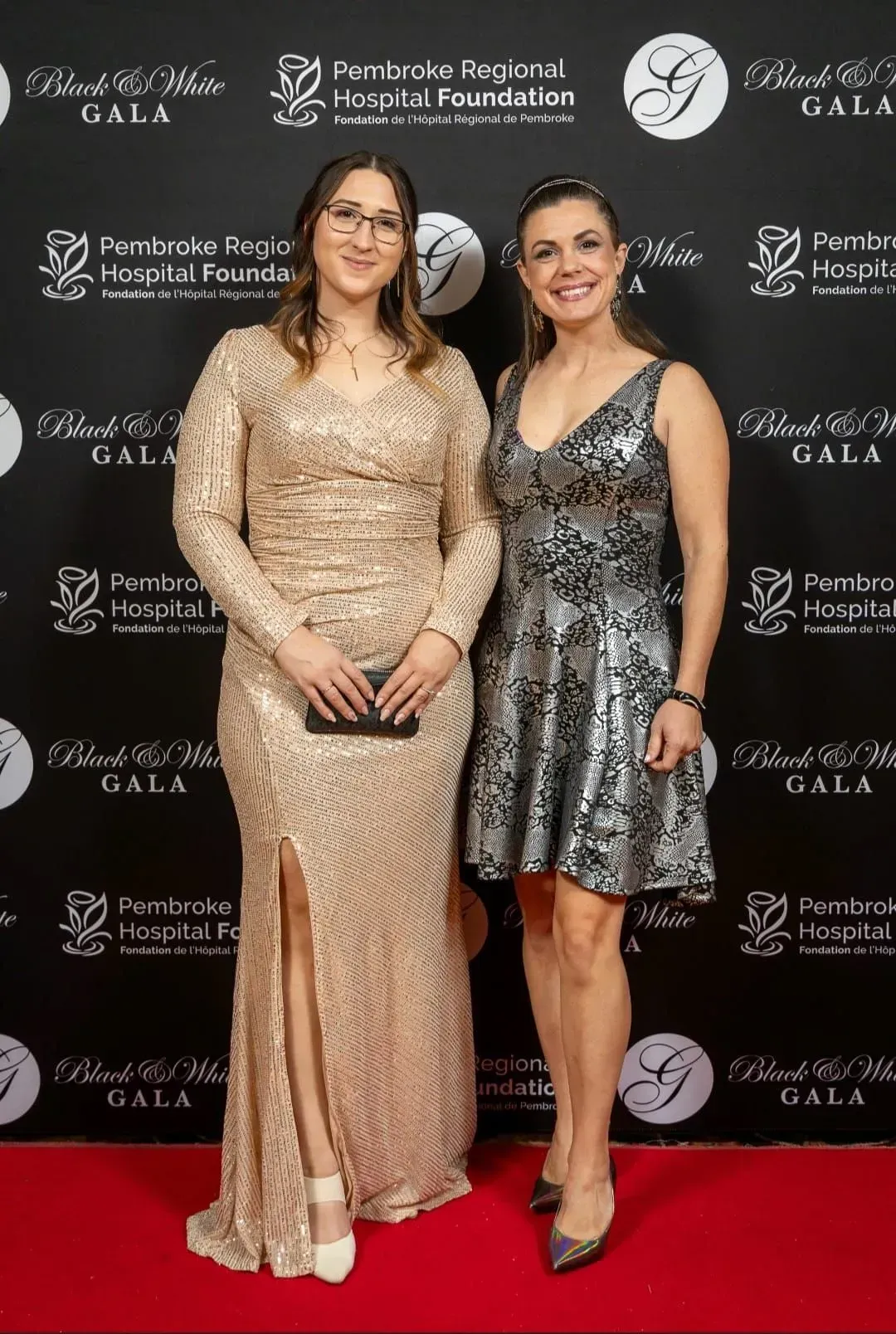 Two women posing on a red carpet in evening gowns at a gala event backdrop.
