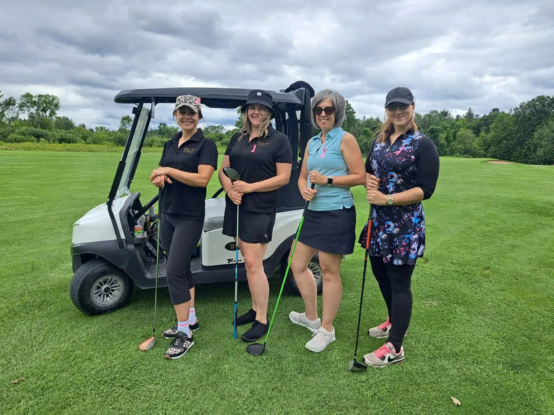 Four people posing beside a golf cart on a green field under a cloudy sky