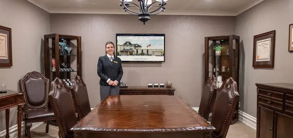 Conference room with a woman standing beside a large wooden table, framed by cabinets and wall art.