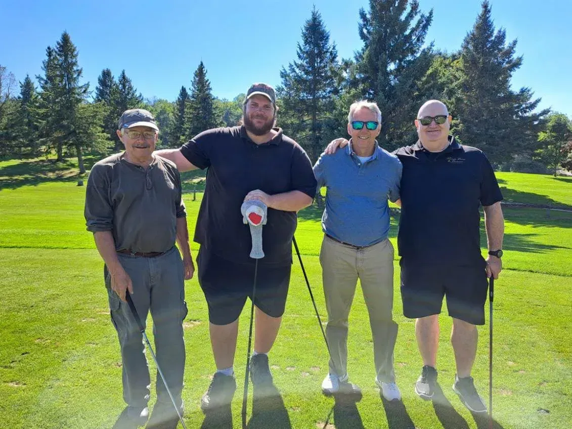 Four people standing on a sunny golf course with trees in the background