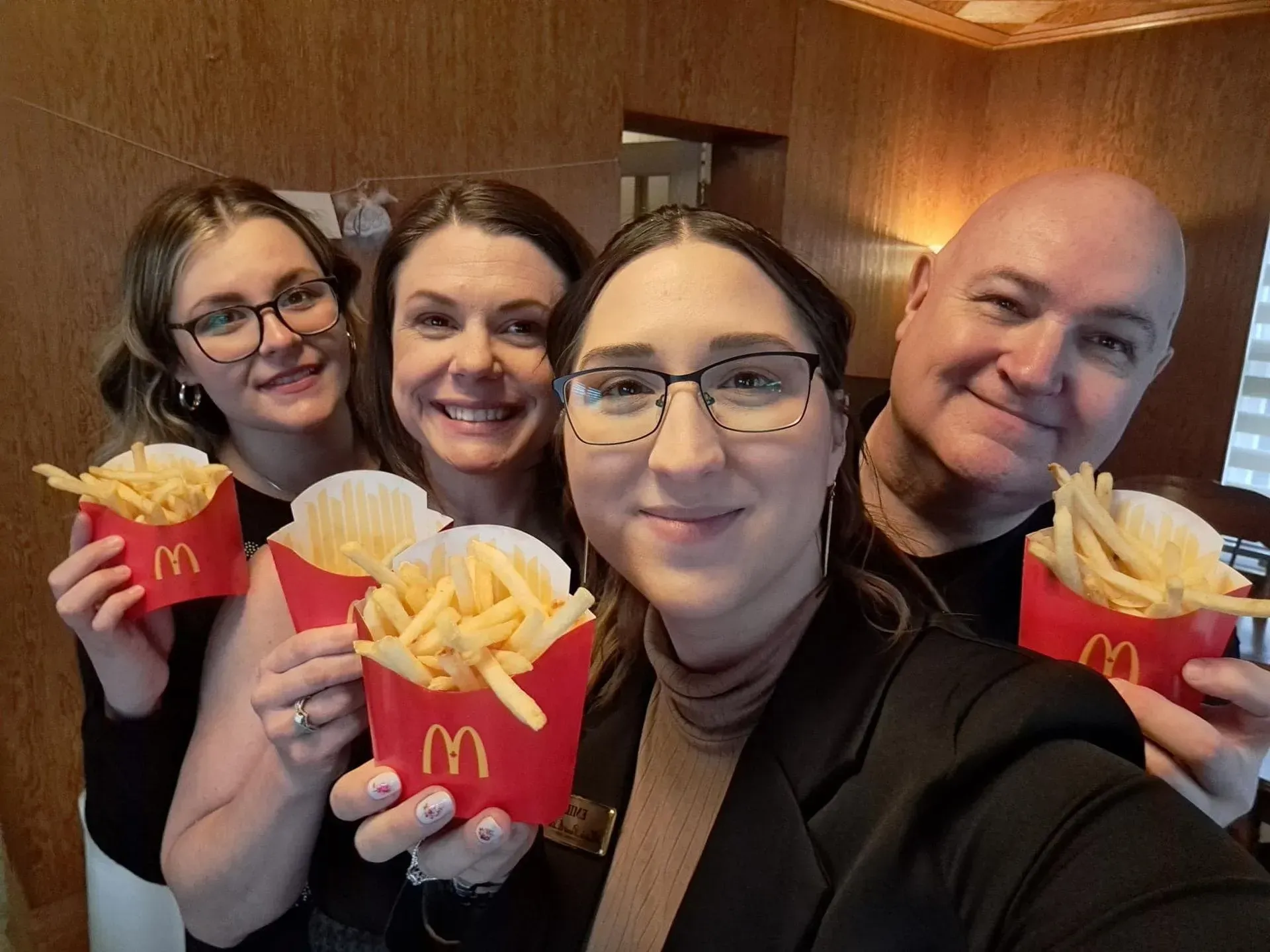 Four people smiling and holding McDonald’s fries in red containers indoors