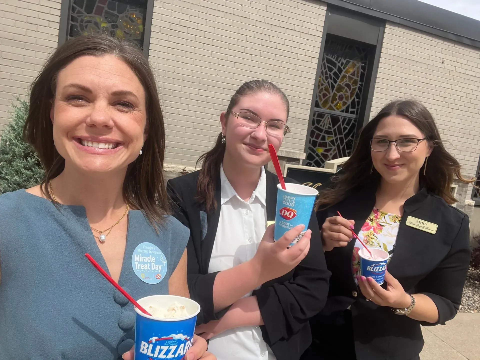 Three smiling people hold drinks and snack cups outdoors in front of a building.