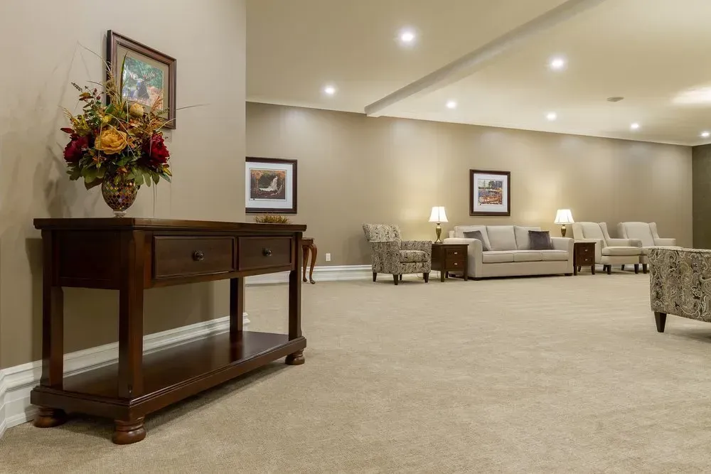 Spacious beige lounge with sofas, lamps, framed art, and a wooden console table with flowers