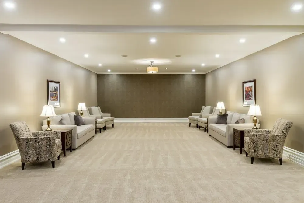Spacious beige waiting room with sofas, armchairs, lamps, and recessed ceiling lights