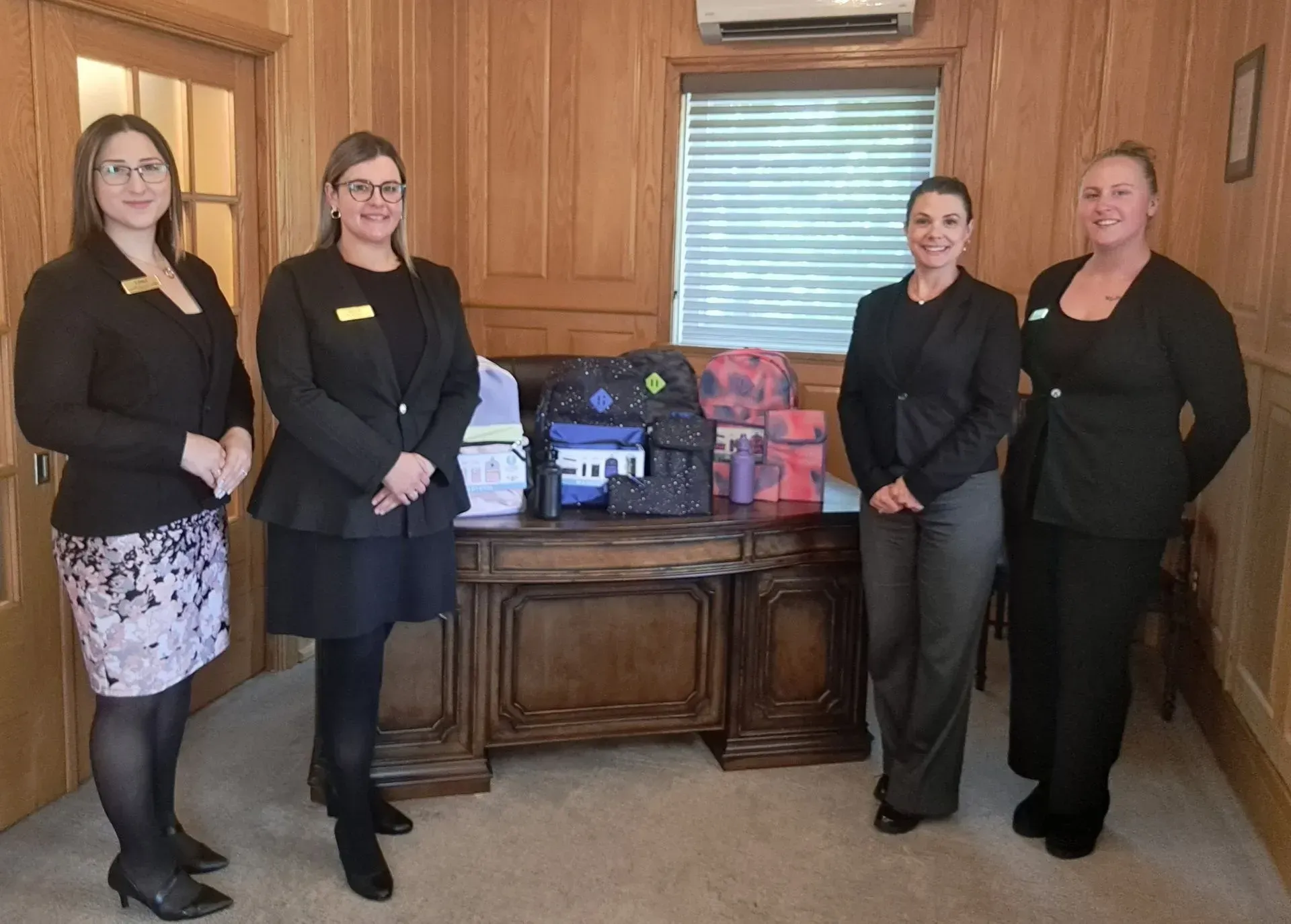 Four people standing beside a table of gift baskets in a wood-paneled room