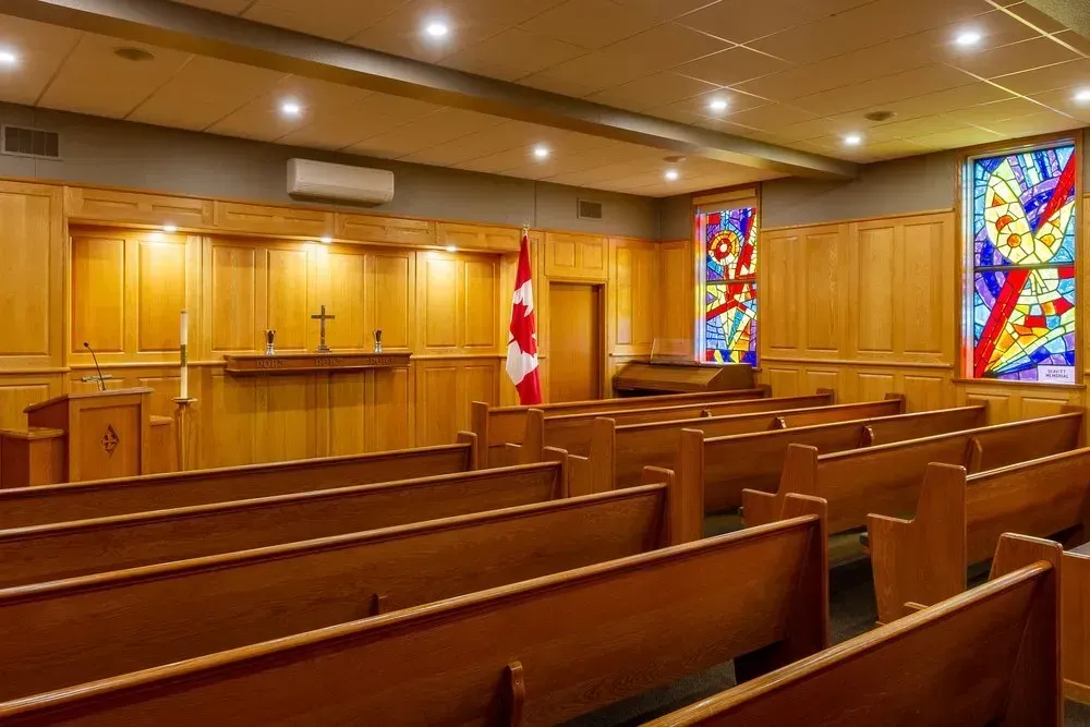 Empty church sanctuary with wooden pews, pulpit, cross, Canadian flag, and stained glass windows