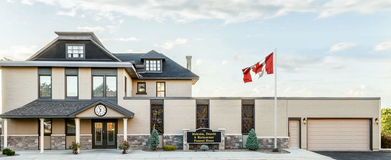 Modern two-story house with stone and siding, three garage doors, and Canadian flags in front