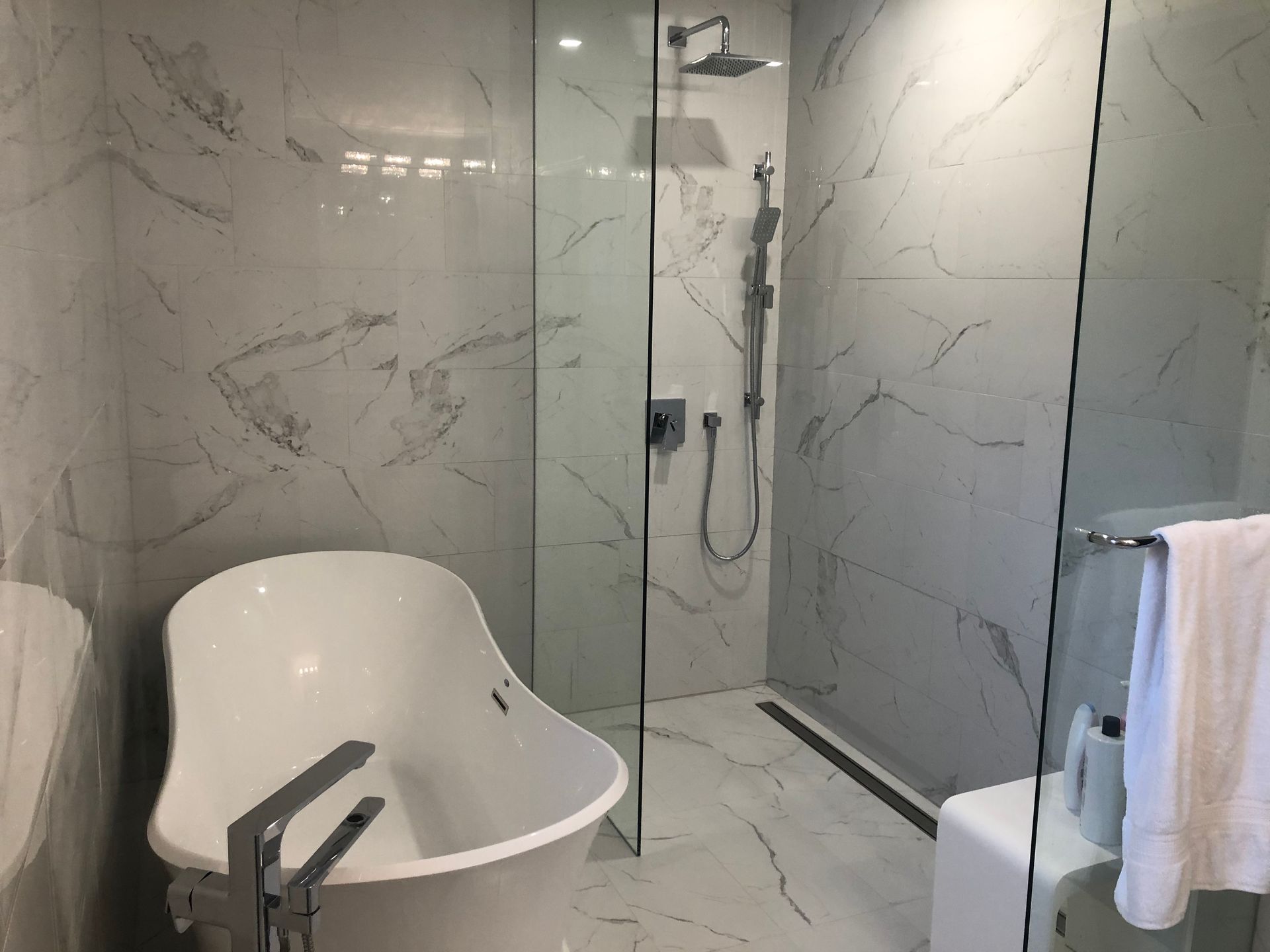 Modern bathroom with marble walls, glass shower, freestanding tub, and towel rack