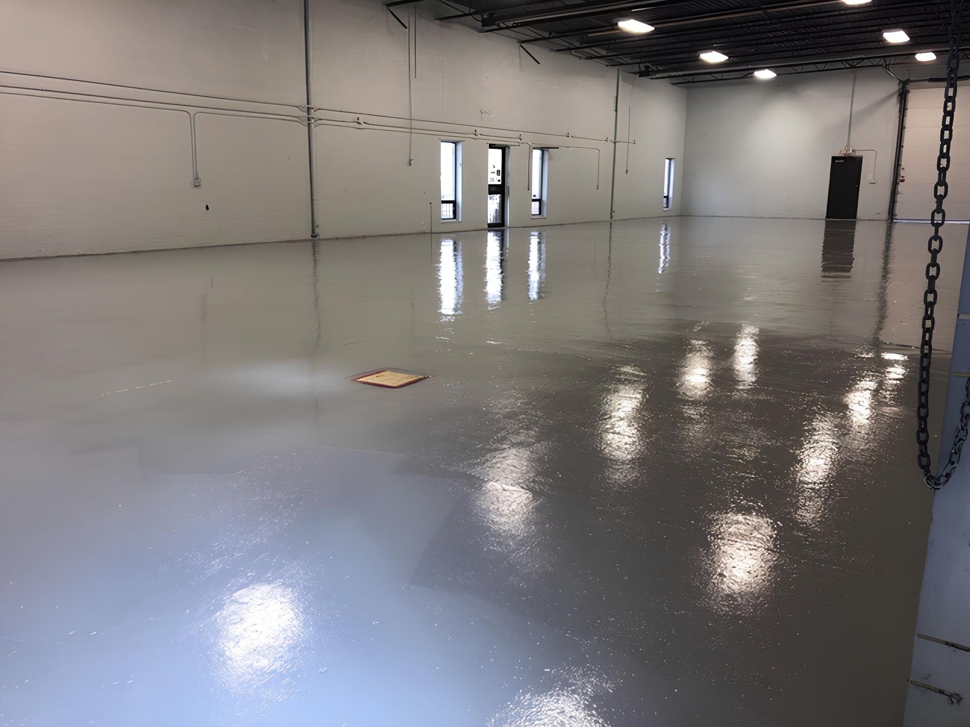 A large, empty, gray-floored room with overhead lights, windows, and a small piece of debris in the center.