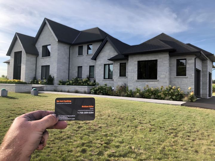A person is holding a business card in front of a large house.