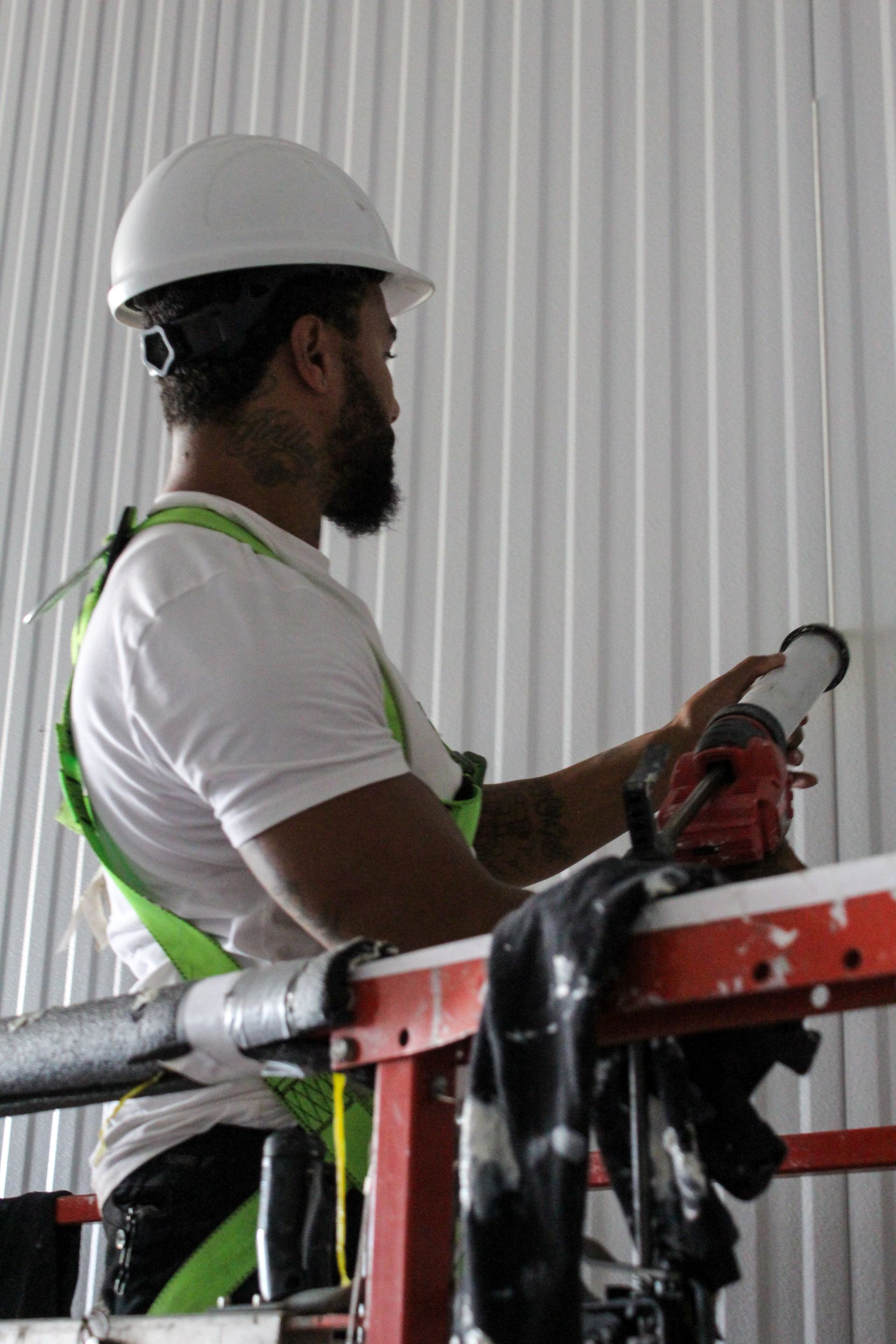 A man wearing a hard hat and safety harness is working on a ladder.