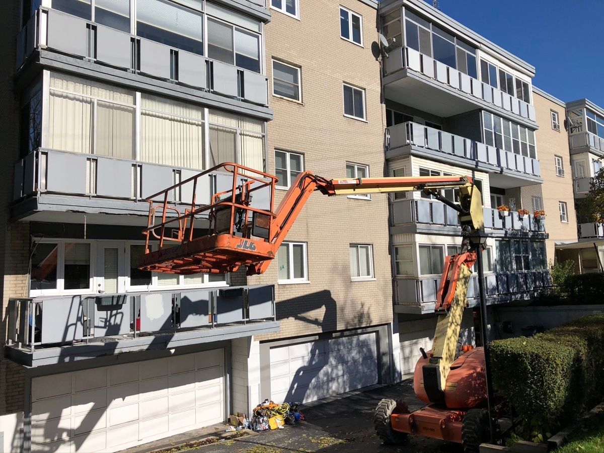 Cherry picker lift beside an apartment building, with a worker reaching the facade for exterior maintenance.