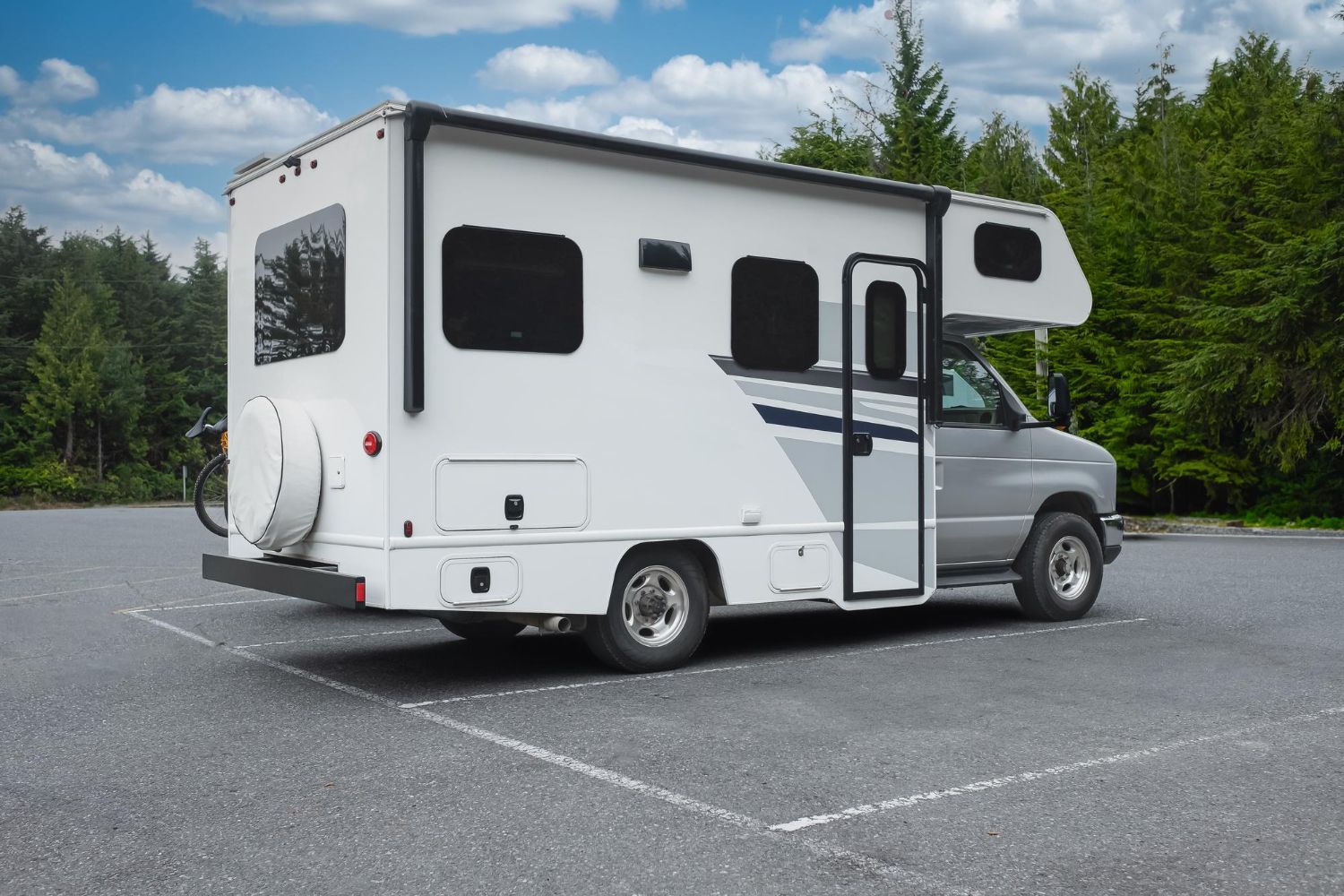 White camper van parked on asphalt with side door open, trees and cloudy sky in the background