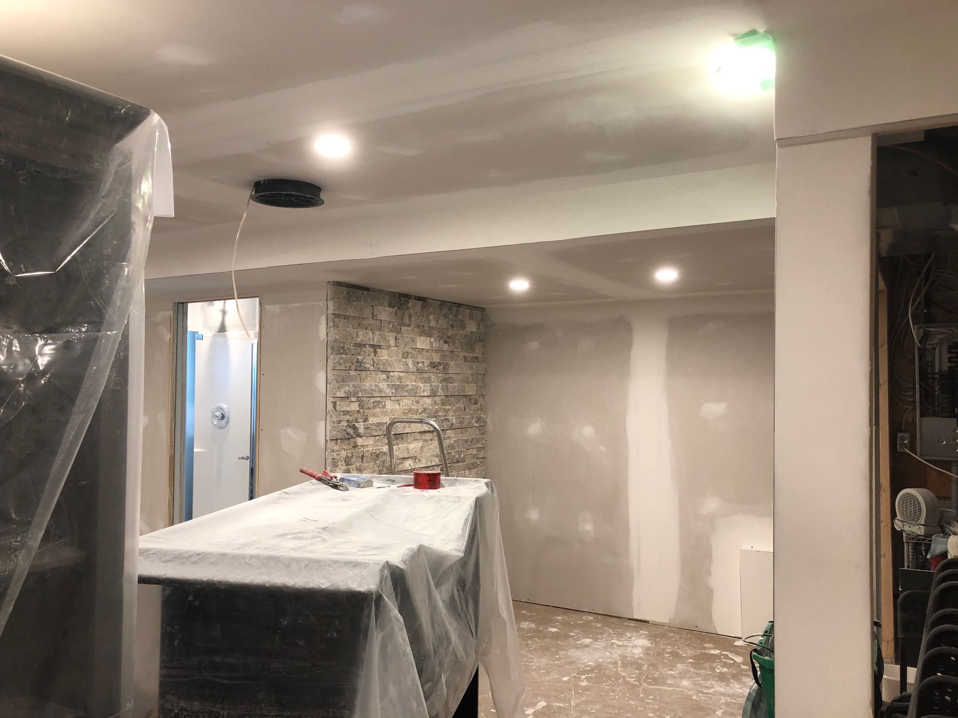 Renovated room with plastic-covered furniture, stone accent wall, and recessed ceiling lights