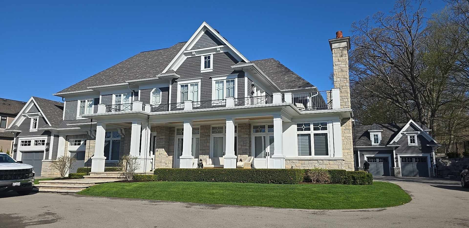 Large gray stone house with white columns, a front porch, and dormer windows on a sunny day