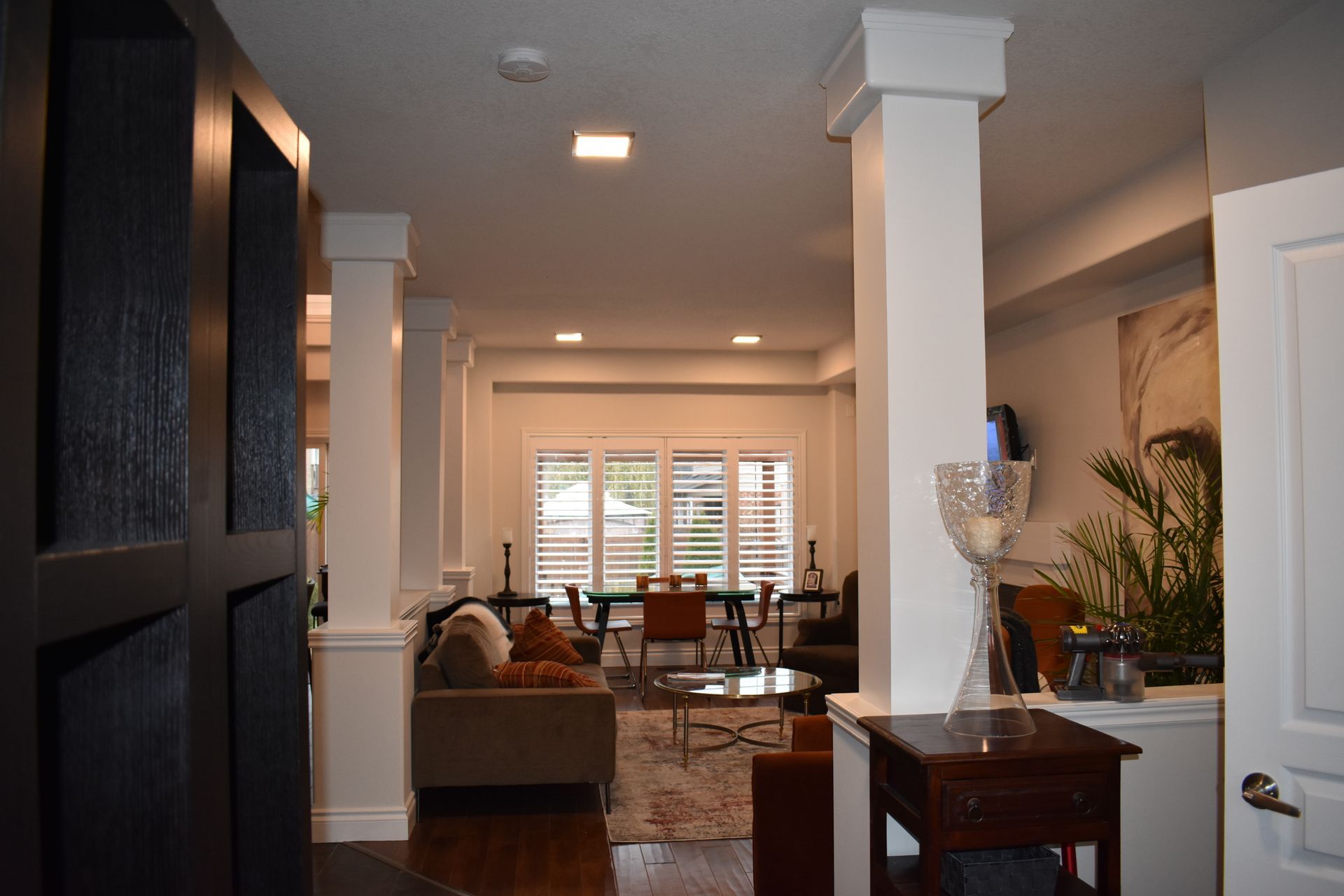 Open-plan living room and dining area with white columns, sofa, table, and large windows.