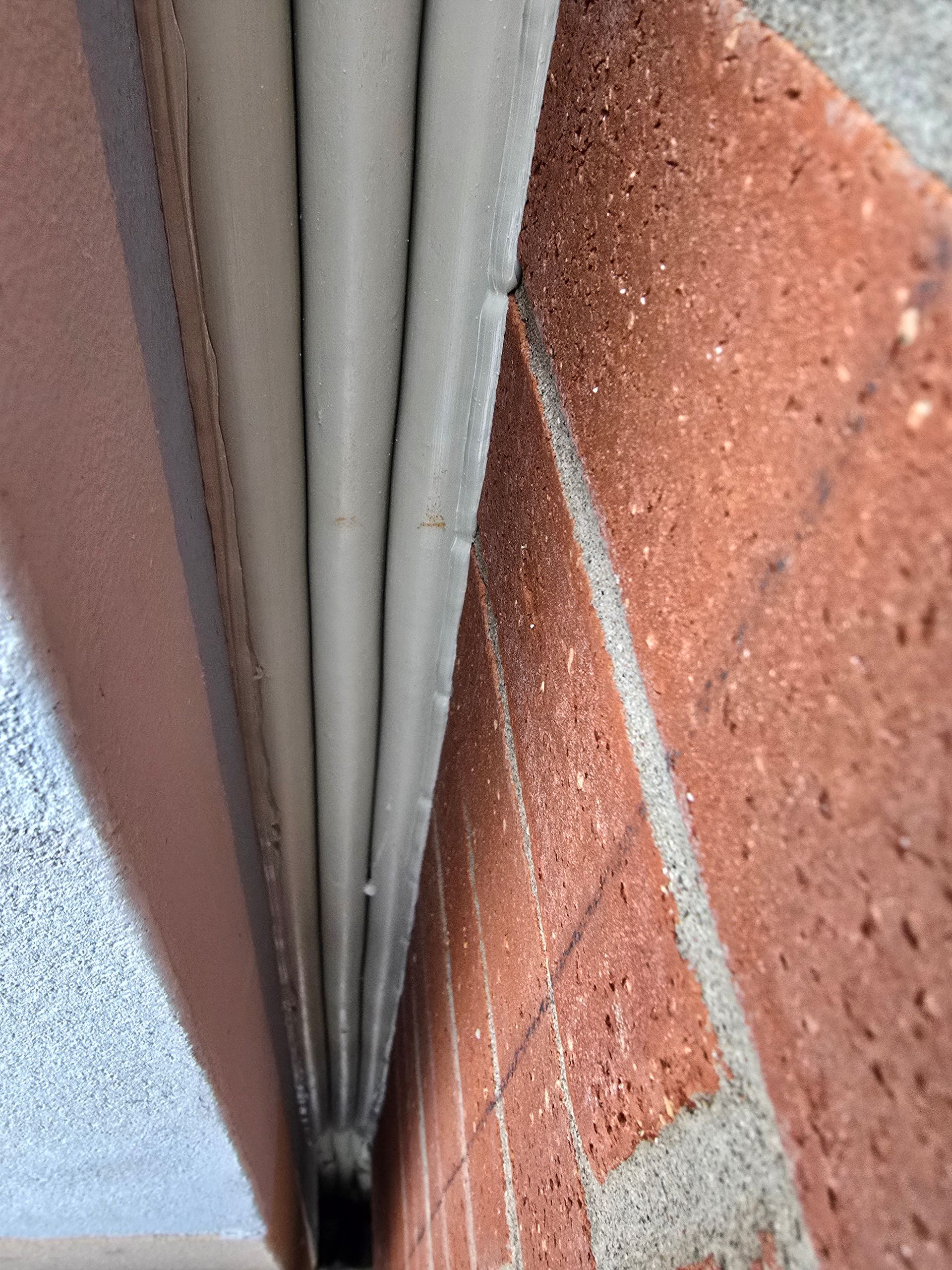 Close-up of a narrow gap between a window frame and a red brick wall, with white sealant visible.