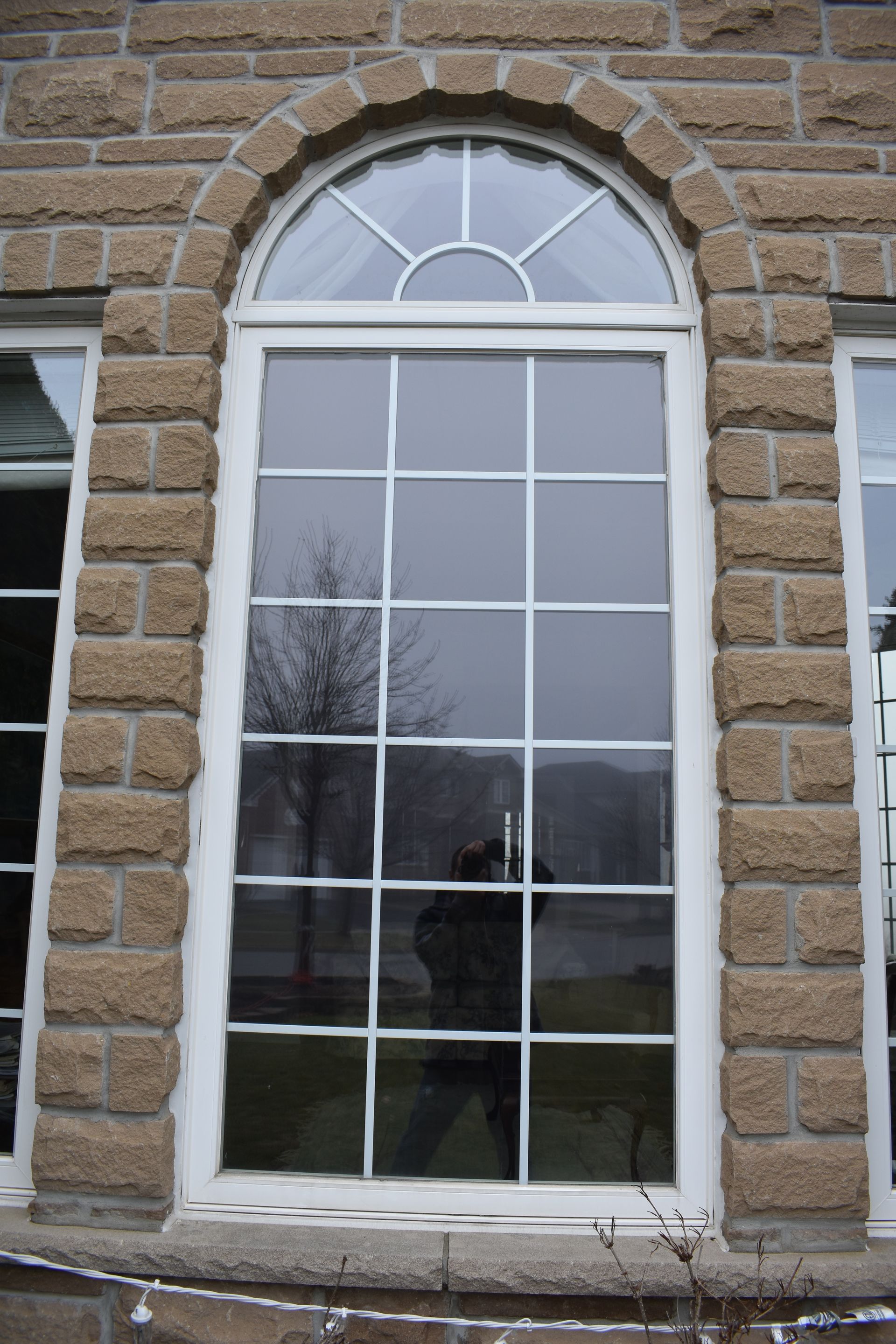 Tall, arched window with white grids set in a rough stone wall. A person is reflected in the glass.