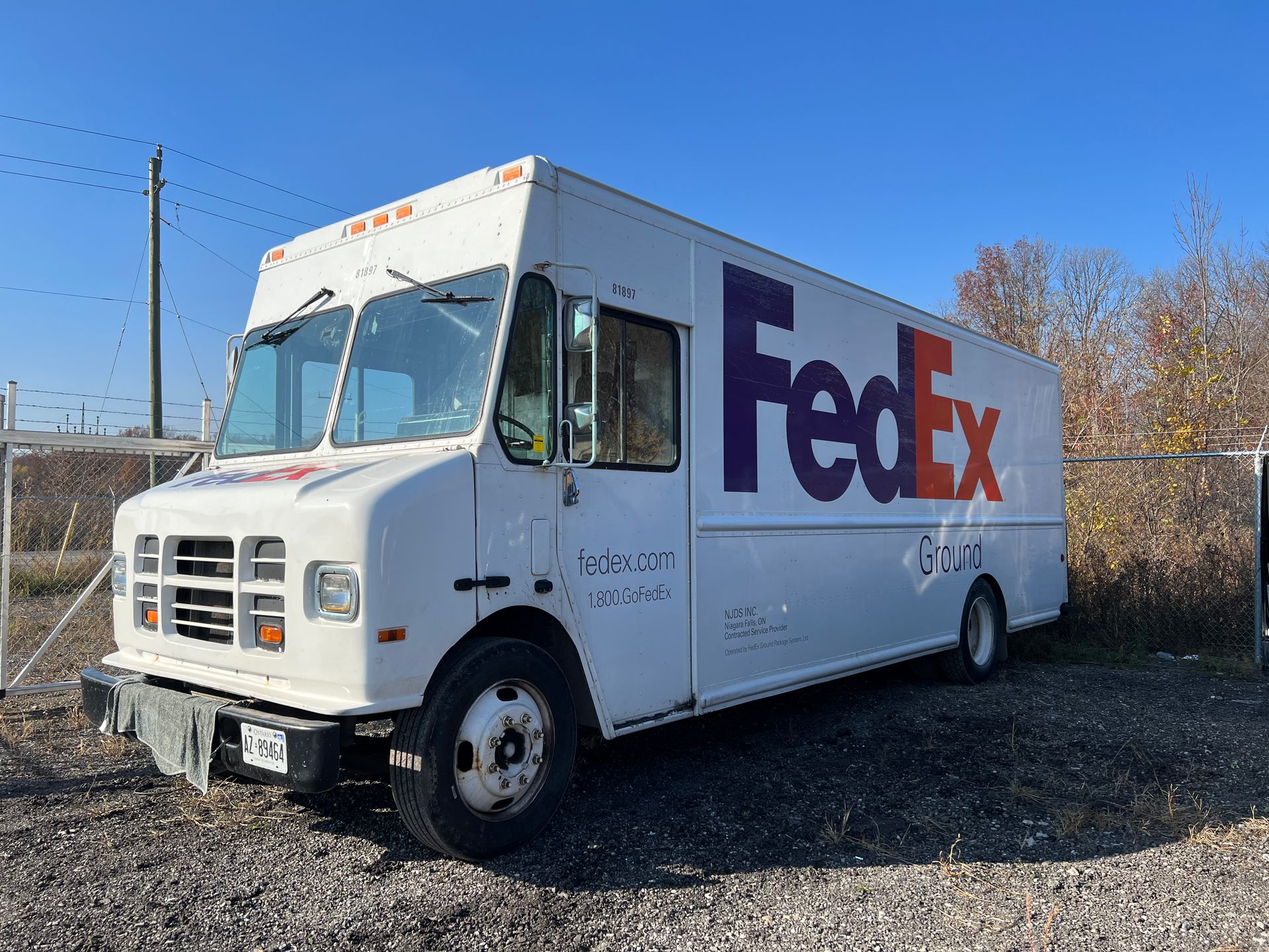 A white fedex truck is parked in a gravel lot.