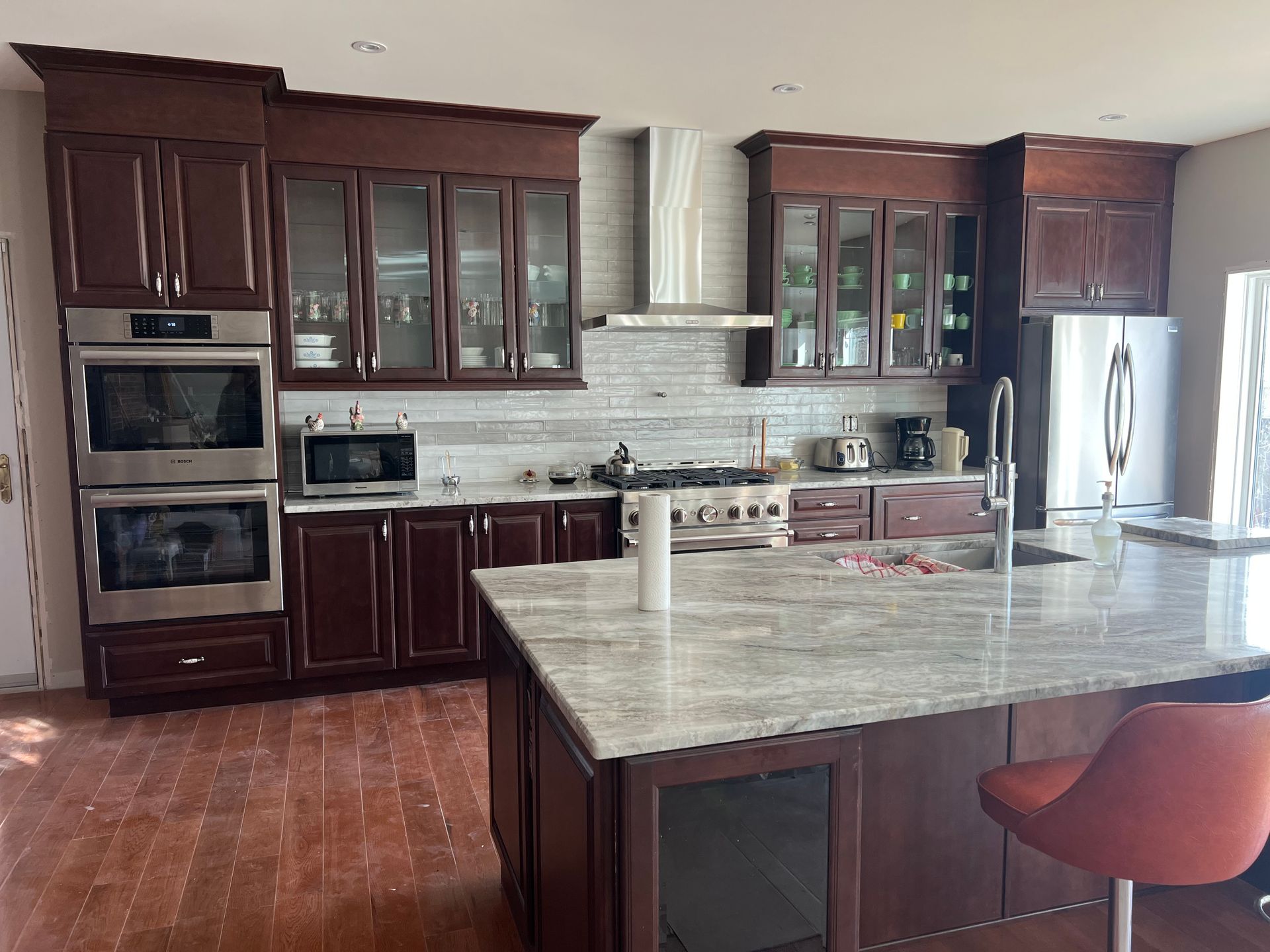 Kitchen with dark wood cabinets, stainless steel appliances, granite island, and red chair.