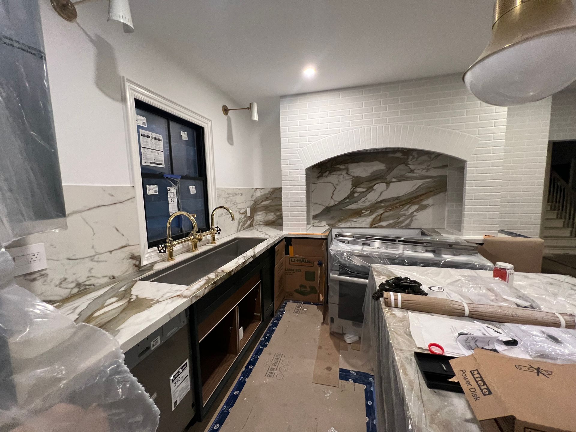 Kitchen under construction, with marble countertops, a brick range hood, and an island.