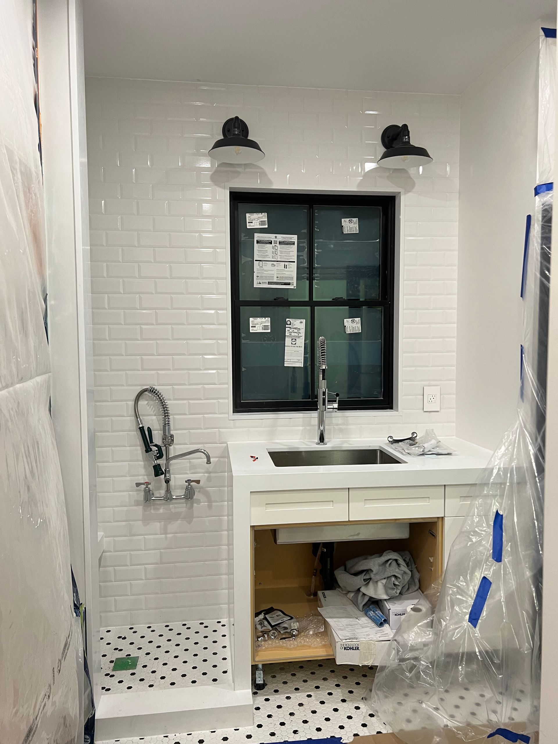 Small white-tiled utility room with a sink under a window and a faucet.
