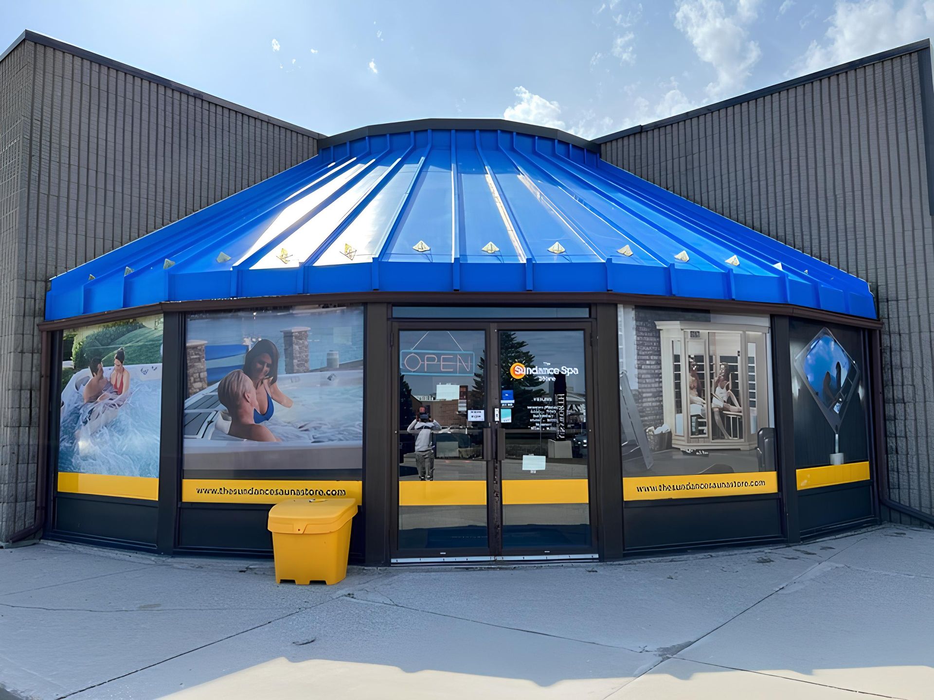 A storefront with a blue roof, yellow trim, and large windows displaying hot tub and spa products.