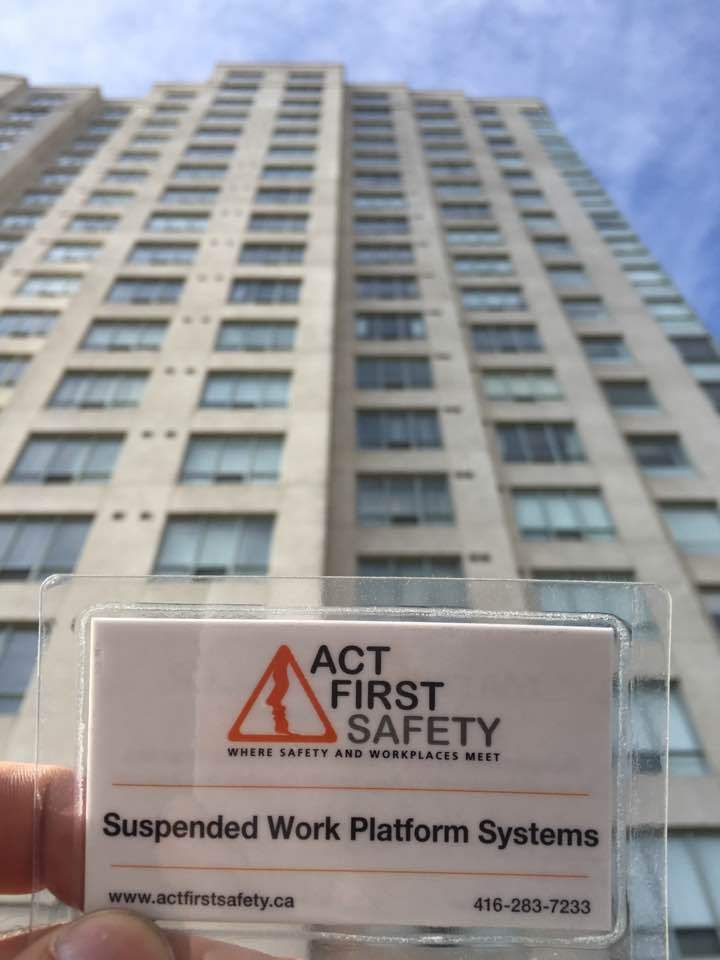 Suspended work platform safety sign held in front of a tall high-rise building.