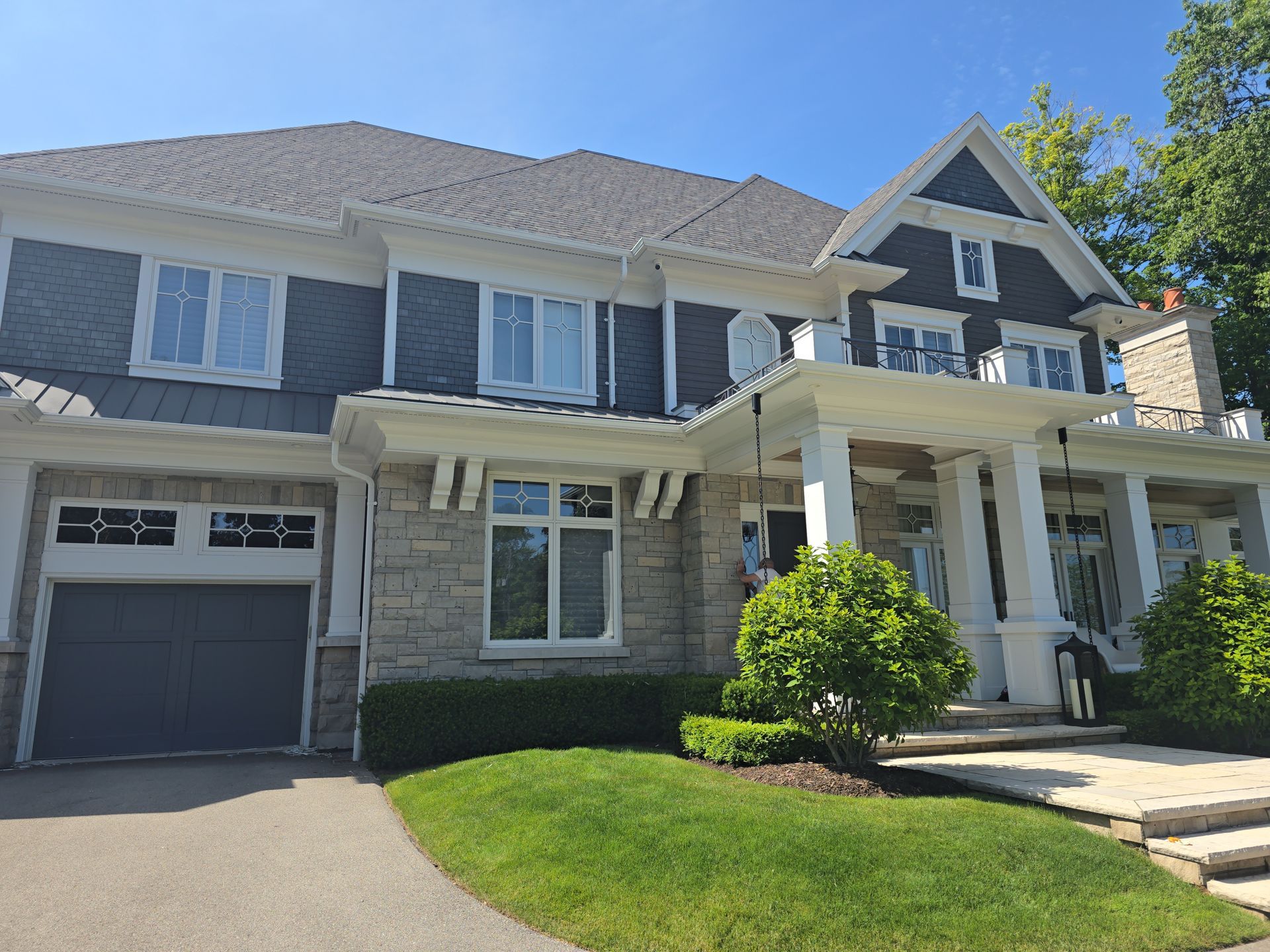 Large two-story suburban house with gray siding, white trim, garage, and front porch on a sunny day