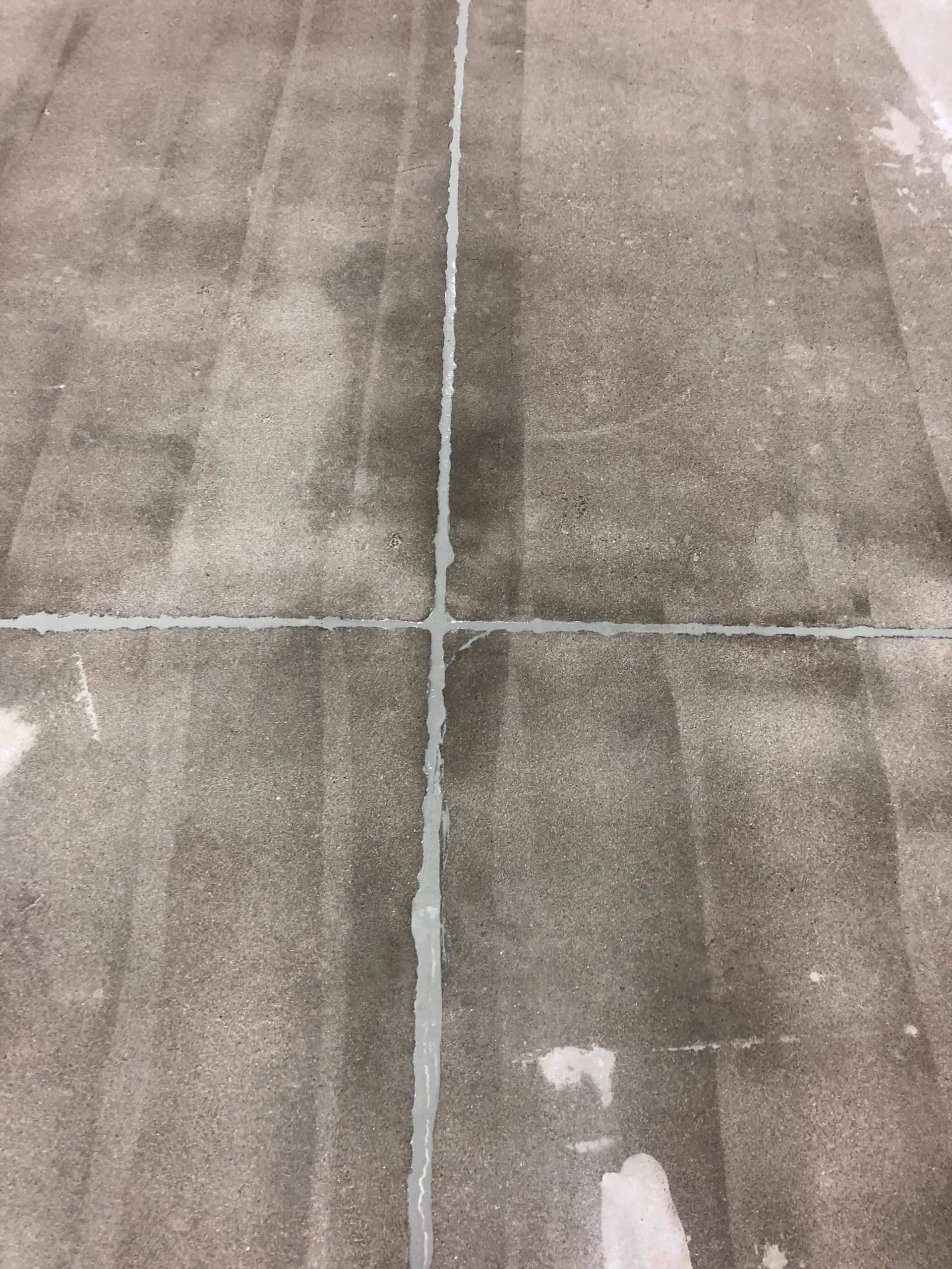 Gray concrete floor with visible seams, forming a cross pattern with a white sealant in the joints.
