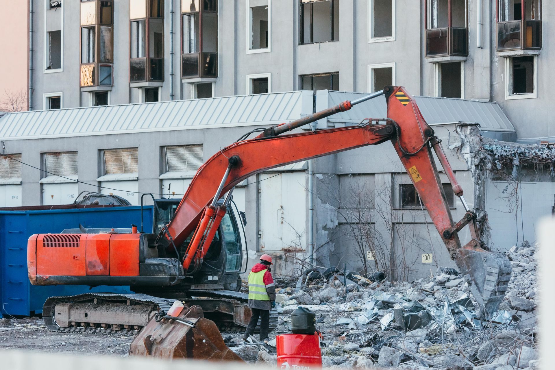 A large orange excavator is demolishing a building on a construction site.