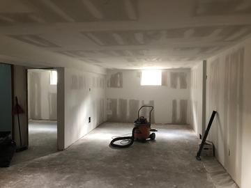 Basement with drywall installed on walls and ceiling, unfinished floor. Wet/dry vacuum in the center.